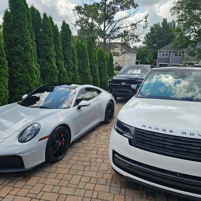A white Porsche 911 and a white Range Rover side by side on a paver driveway