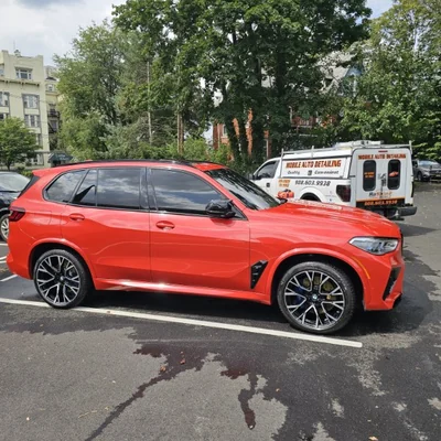 A red BMW X5 M with the Rashine Mobile Auto Detailing van parked behind it