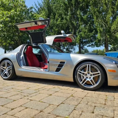 A silver Mercedes-Benz SLS AMG with its gullwing doors open on a paver driveway after detailing