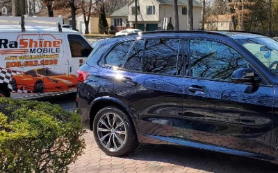 A black BMW X5 on a paver driveway with the Rashine Mobile van behind it